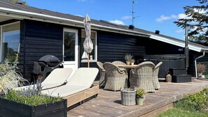 Ein modernes Haus mit Terrasse, Gartenmöbeln und einem großen Fenster.