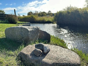 Une rivière aux eaux calmes, bordée d’herbe et de gros rochers.