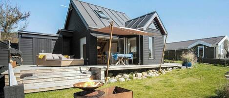 A modern house with a deck, a fire pit, and a covered patio area.