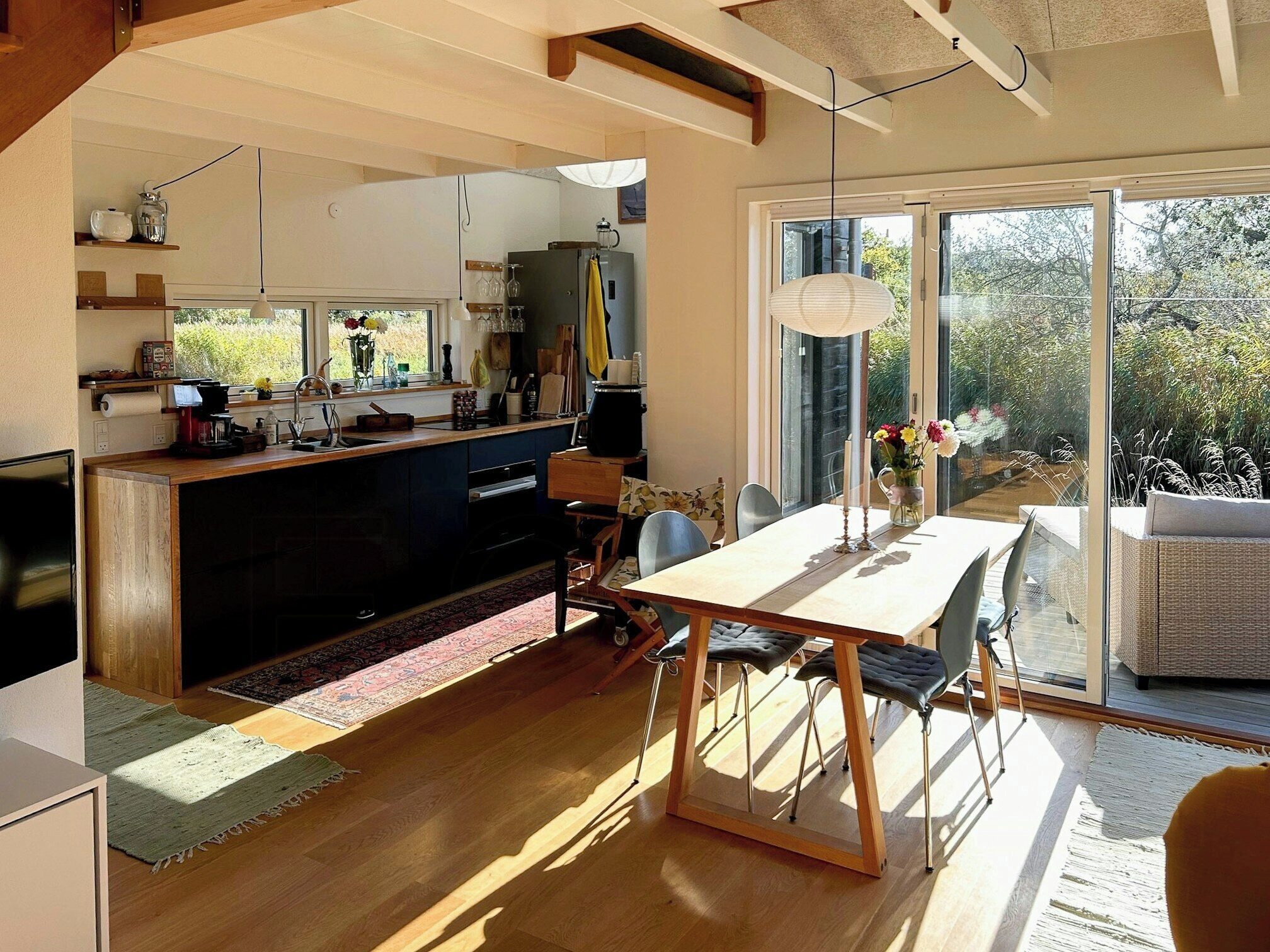 A modern kitchen with a dining area, large windows, and a view of greenery.