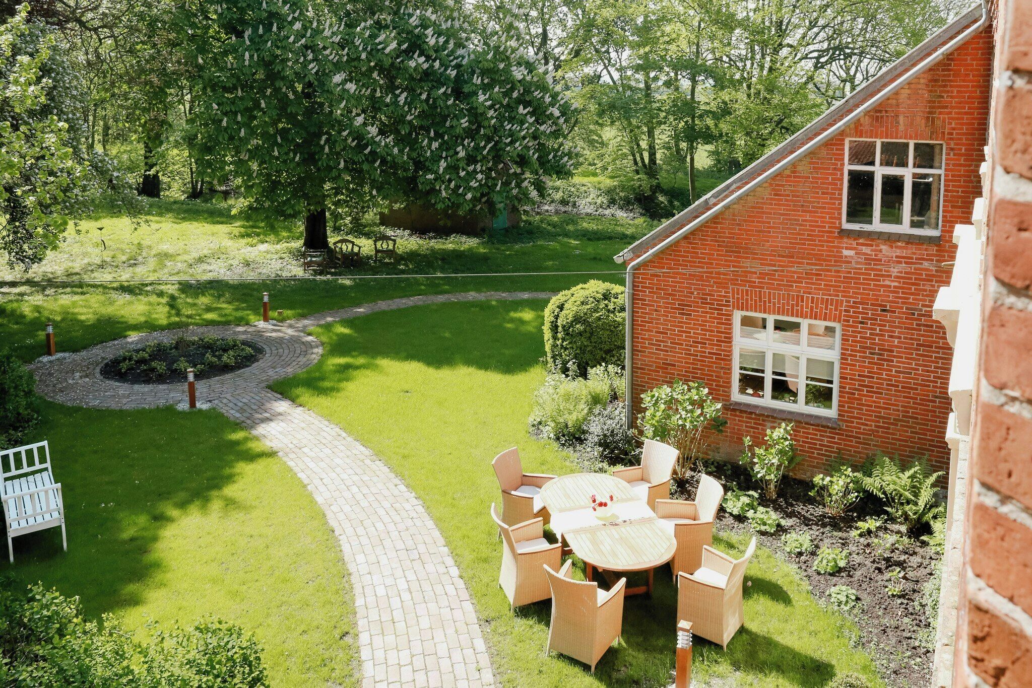 A brick house with a garden, a paved pathway, and outdoor furniture.