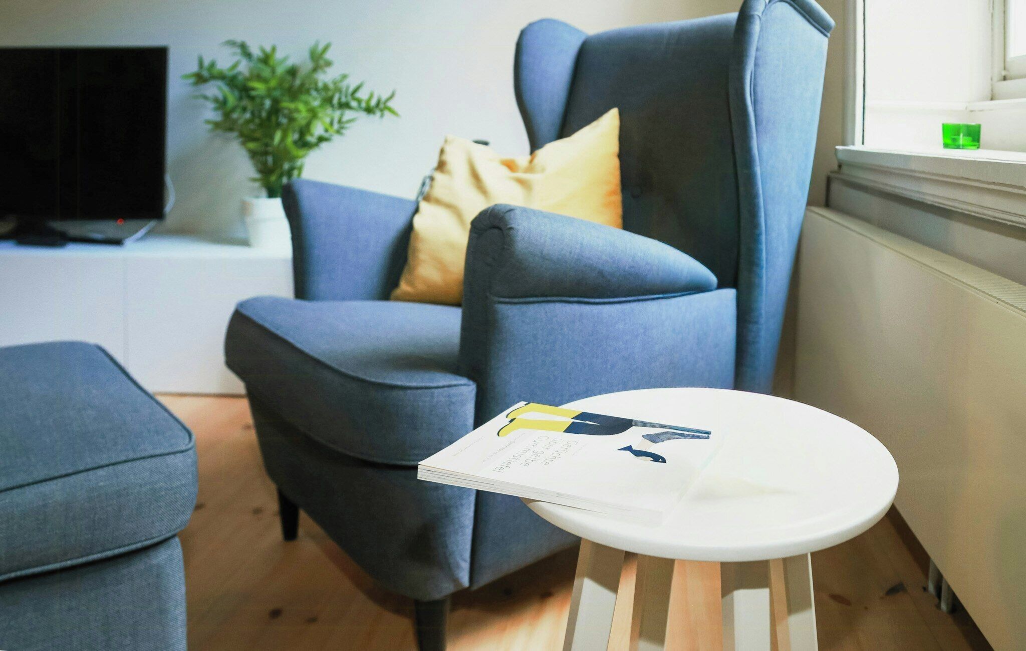 A modern living room with a blue armchair, a small white table, and a potted plant.