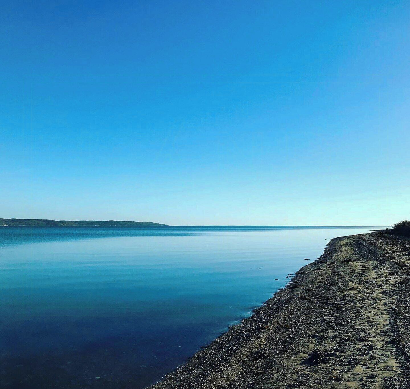Eine Küstenlandschaft mit ruhiger See, felsiger Küste und einer entfernten Landmasse.