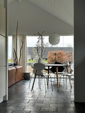 Un comedor moderno con una mesa, sillas, una lámpara colgante y vistas a través de un ventanal.