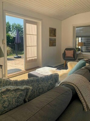 Ein Wohnzimmer mit Sofa, Sessel, Lampe und Blick durch eine Glastür.