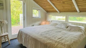 Un dormitorio con una cama grande, techo de madera y vistas al verdor exterior.