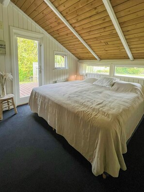 Ein Schlafzimmer mit einem großen Bett, Holzboden und Blick auf Grün.