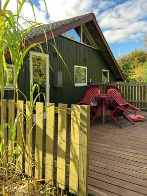 Eine Holzterrasse mit einem grünen Gebäude, zwei roten Stühlen und einem Holzzaun.