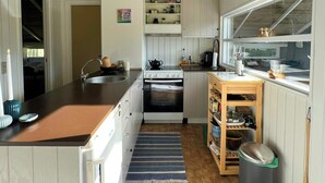 Una cocina con gabinetes de madera, una estufa, un lavamanos y un ventanal con vistas al jardín trasero.