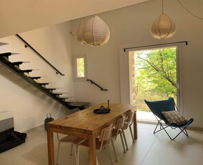 Ein modernes Interieur mit einem Holztisch, weißen Stühlen, einem blauen Klappstuhl, einer Treppe mit schwarzen Geländern und zwei hängenden Papierlampen.