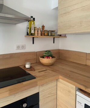 Eine Küche mit Holzarbeitsplatte, einem schwarzen Induktionskochfeld, einer Holzküche mit Früchten und einem Regal mit Küchenutensilien.