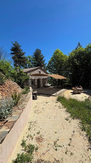 Ein Steinhhaus mit Terrasse, Gartenmöbeln und einem Kiesweg.