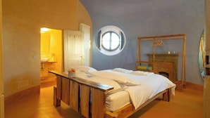 A bedroom with a wooden bed, a round window, a fireplace, and a door leading to another room. - Historic tower with Monferrato views (Terrugia)