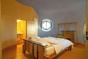 A bedroom with a wooden bed, a round window, a fireplace, and a door leading to another room.