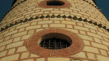 Une haute tour cylindrique en briques, dotée de fenêtres rondes et surmontée d’un toit en forme de pyramide.