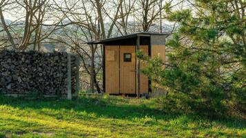 Eine kleine Holzhütte mit geneigtem Dach, gelegen in einer grünen Wiese mit Bäumen im Hintergrund.
