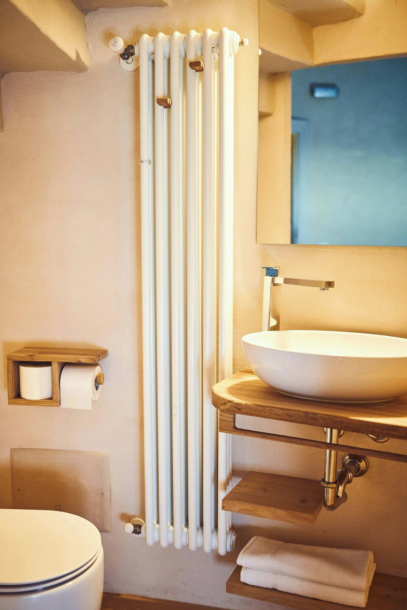 A bathroom with a toilet, a sink, a mirror, a towel rack, and a radiator.