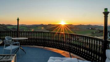 Ein Balkon mit Blick auf den Sonnenuntergang, eine weiße Sitzgelegenheit mit Kissen und ein Metallgeländer.
