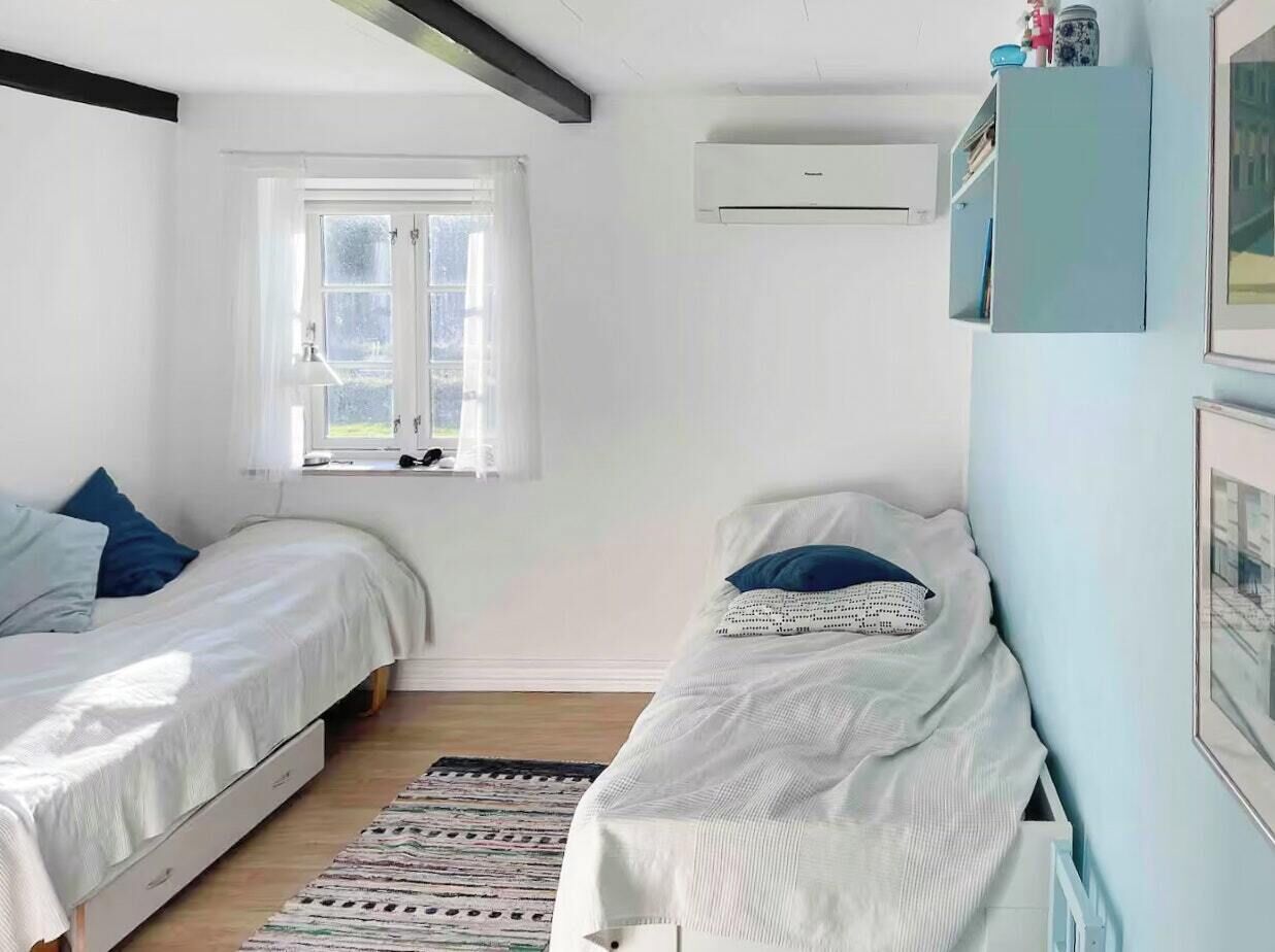 Ein Schlafzimmer mit zwei Einzelbetten, einem Fenster, einer Klimaanlage und einem Regal mit Gegenständen.