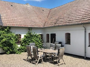 Une cour avec un bâtiment blanc, une table entourée de chaises et un barbecue.