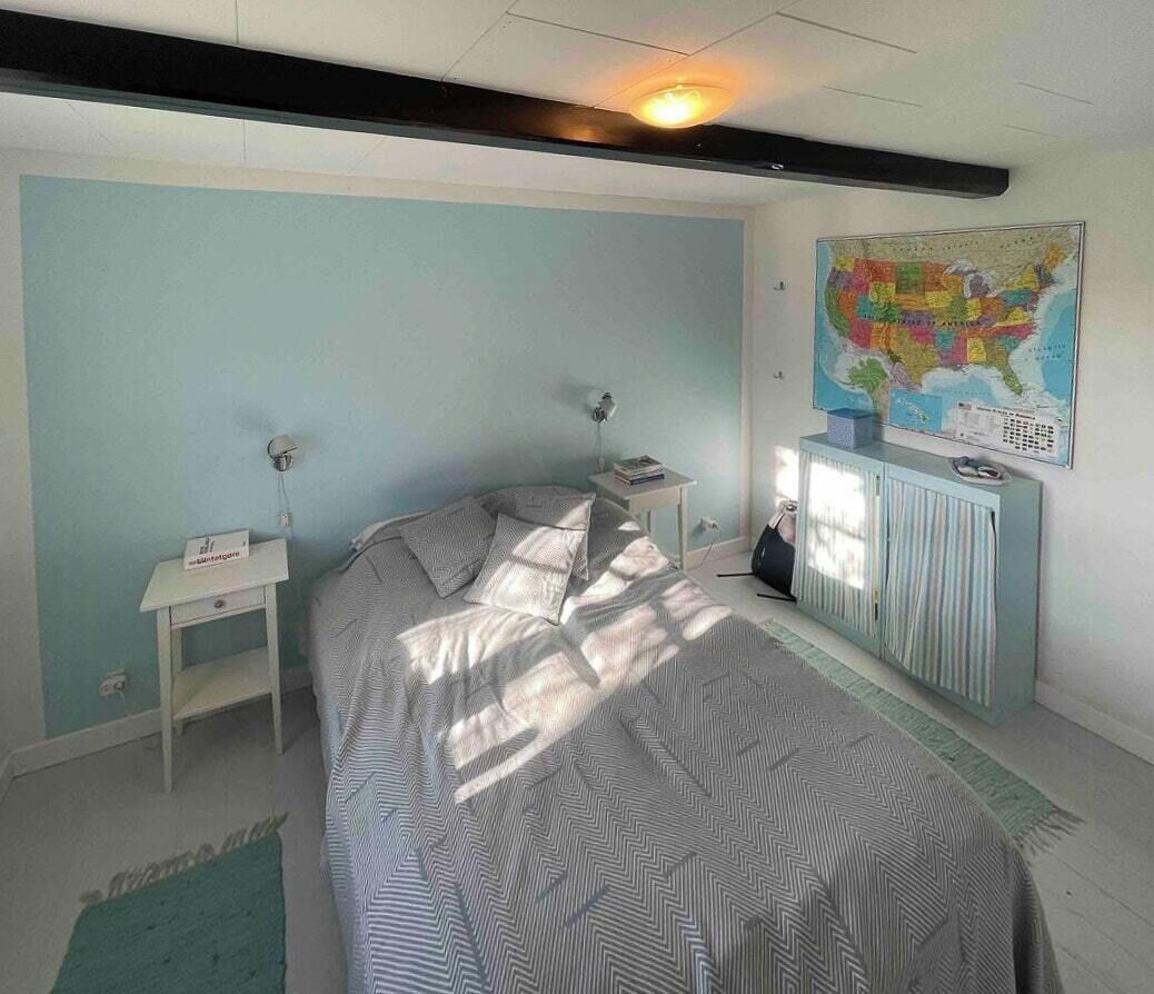 A bedroom with a bed, a nightstand, a dresser, a map on the wall, and a window.