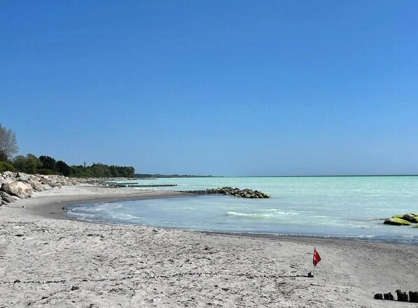 Une plage avec un ciel dégagé, une mer calme et un rivage rocheux.