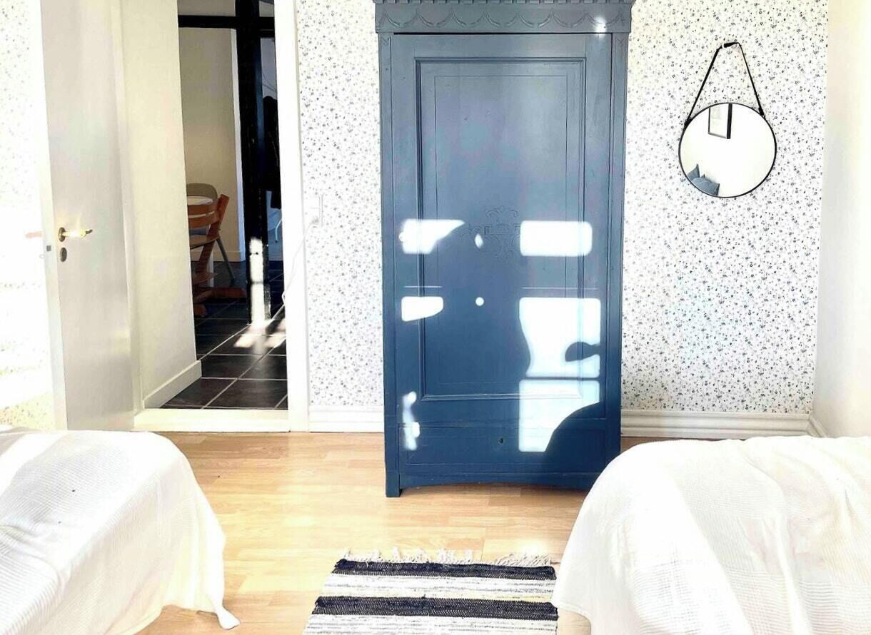Una habitación con una puerta, una cama, un tapete y una lámpara fijada a la pared.