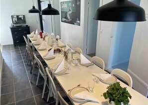 Une longue table à manger, recouverte de nappes blanches, illuminée par des suspensions noires et agrémentée de chaises disposées avec soin.