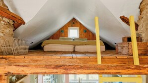 A loft bedroom with a sloped ceiling, wooden beams, a window, and a bed.
