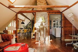 Habitación estilo loft con vigas de madera a la vista, pared de piedra y zona de comedor con sillas amarillas.