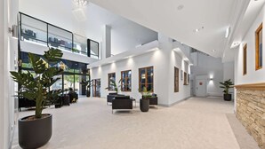 A spacious lobby with a high ceiling, large windows, and potted plants.