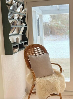 Ein Korbstuhl mit weichem Sitz und Kissen, neben einem an der Wand befestigten Regal mit Keramiktassen.