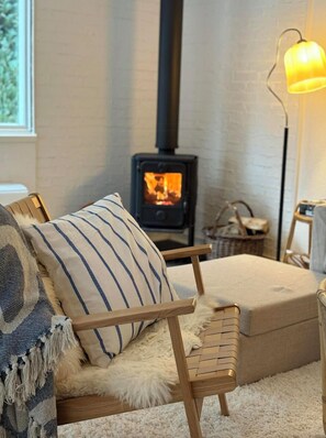 Ein gemütliches Wohnzimmer mit einem Holzstuhl, einem flauschigen Teppich, einem gestreiften Kissen, einem kleinen Tisch und einer Wandlampe.