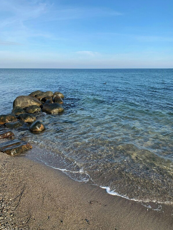 Ein Strand mit klarem Wasser, Felsen und Kies.