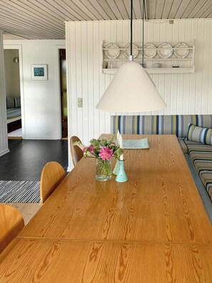 Ein Essbereich mit einem Holztisch, Stühlen, einer Blumenvase, einer Hängelampe und einem gestreiften Sofa.