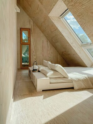 A bedroom with a sloped ceiling, a skylight, a bed, a bedside table, and a nightstand.