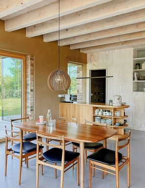 A modern kitchen with a wooden table and chairs, a hanging light fixture, and a brick wall.