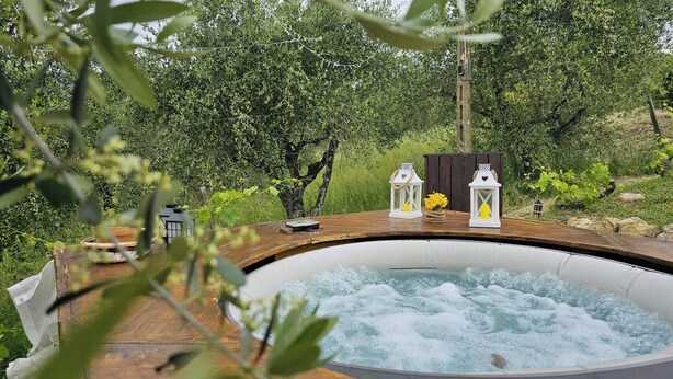 Una vasca idromassaggio circondata dal verde, con un pontile in legno e due lanterne bianche.