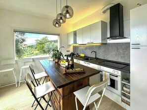 A modern kitchen with a central island, white cabinetry, a black range hood, and a view of greenery outside. - Panoramic villa in the Lucca hills (Capannori)