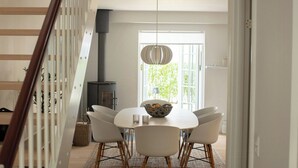 A dining area with a white table, four chairs, a hanging light fixture, and a view of a window with greenery outside. - House in Rørvig Park filled with charm (Bysted)