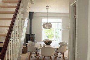 A dining area with a white table, four chairs, a hanging light fixture, and a view of a window with greenery outside. - House in Rørvig Park filled with charm (Bysted)