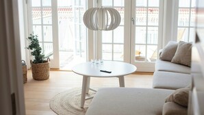 A modern living room with a sofa, a round table with glasses, and a hanging light fixture. - House in Rørvig Park filled with charm (Bysted)