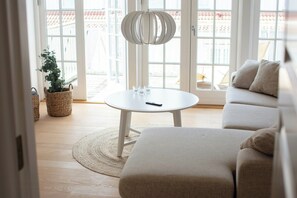A modern living room with a sofa, a round table with glasses, and a hanging light fixture. - House in Rørvig Park filled with charm (Bysted)