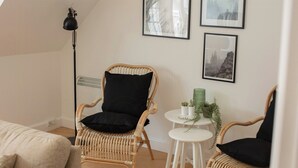 A room with a rattan chair, a small white table with a plant, and framed pictures on the wall. - House in Rørvig Park filled with charm (Bysted)