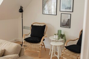 A room with a rattan chair, a small white table with a plant, and framed pictures on the wall. - House in Rørvig Park filled with charm (Bysted)