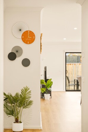 Un couloir orné d’horloges murales, avec une plante en pot, et donnant sur un coin repas.