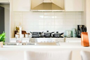 A kitchen with white tiles, a stove, pots, a kettle, and a coffee maker. - Seednest Stylish & Perfect for Relaxation (Weir Views)