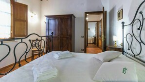 A hotel room with a bed, a wooden wardrobe, a chair, and a nightstand with a lamp. - Apartment with views of Lake Trasimeno (Castiglione del Lago)