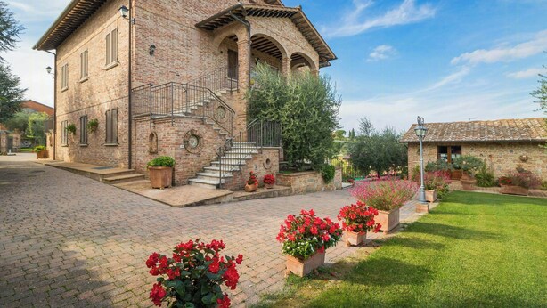 A brick building with a staircase, a garden with red flowers, and a clear blue sky. - Apartment with views of Lake Trasimeno (Castiglione del Lago)