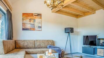 Ein modernes Wohnzimmer mit Sofa, Couchtisch, einer Deckenleuchte, einem Gemälde, einer Stehlampe und einem Fernseher.